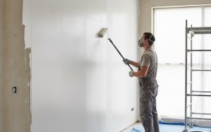 Un bricoleur utilisant un rouleau pour appliquer de l'enduit sur un mur intérieur.