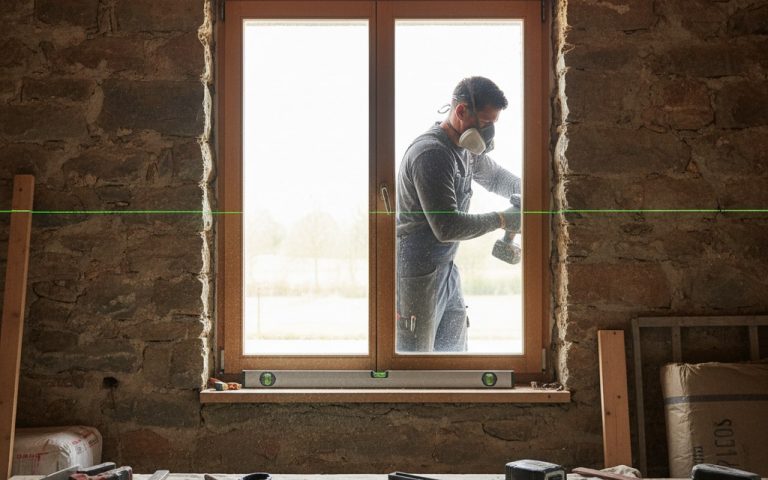 Artisan posant une fenêtre en applique sur un mur avec des outils de mesure.
