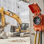 Prise 5 broches installée sur un mur de chantier avec équipements industriels en arrière-plan.